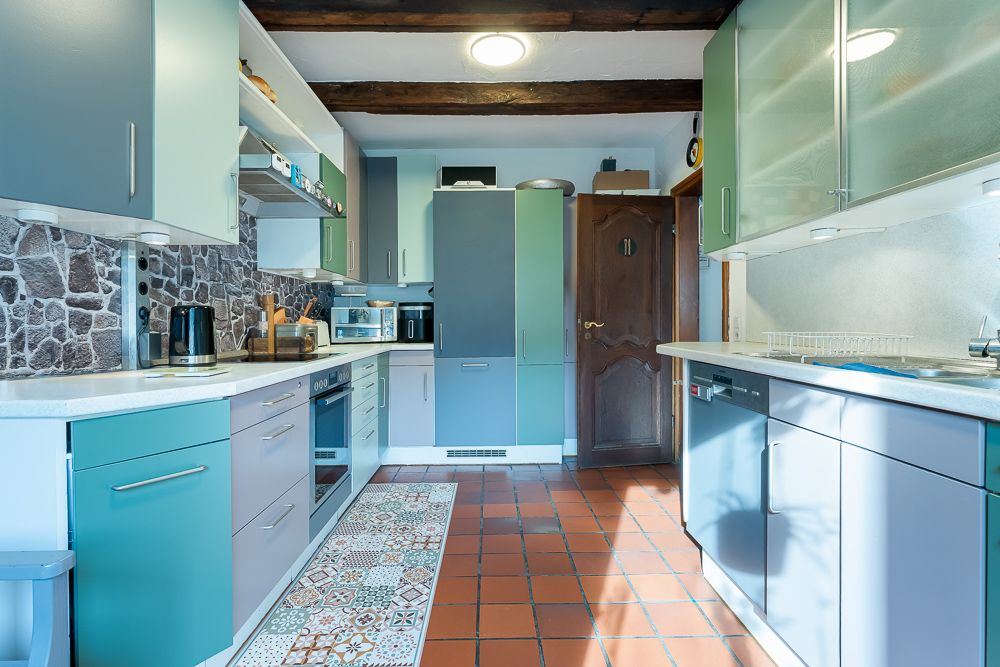 Helle Küche mit blauen Schränken, Steinwand, Keramikboden und Holzbalken an der Decke.