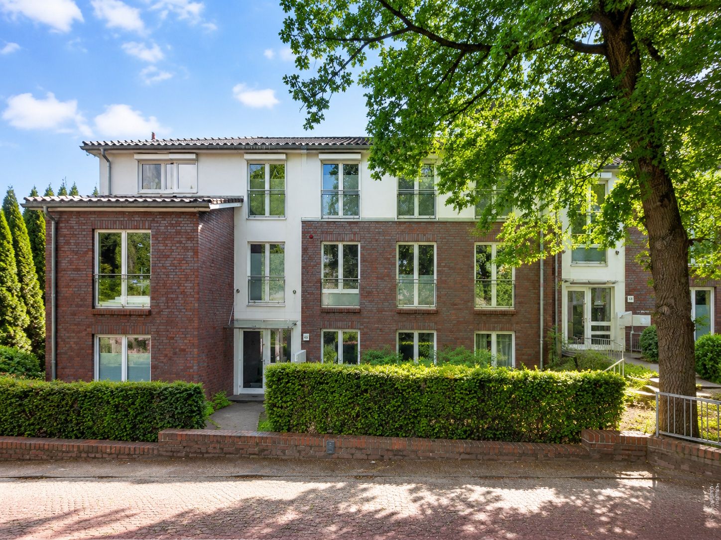 Dreistöckiges Wohnhaus mit Ziegel- und weißen Fassaden, großen Fenstern und Bäumen davor.