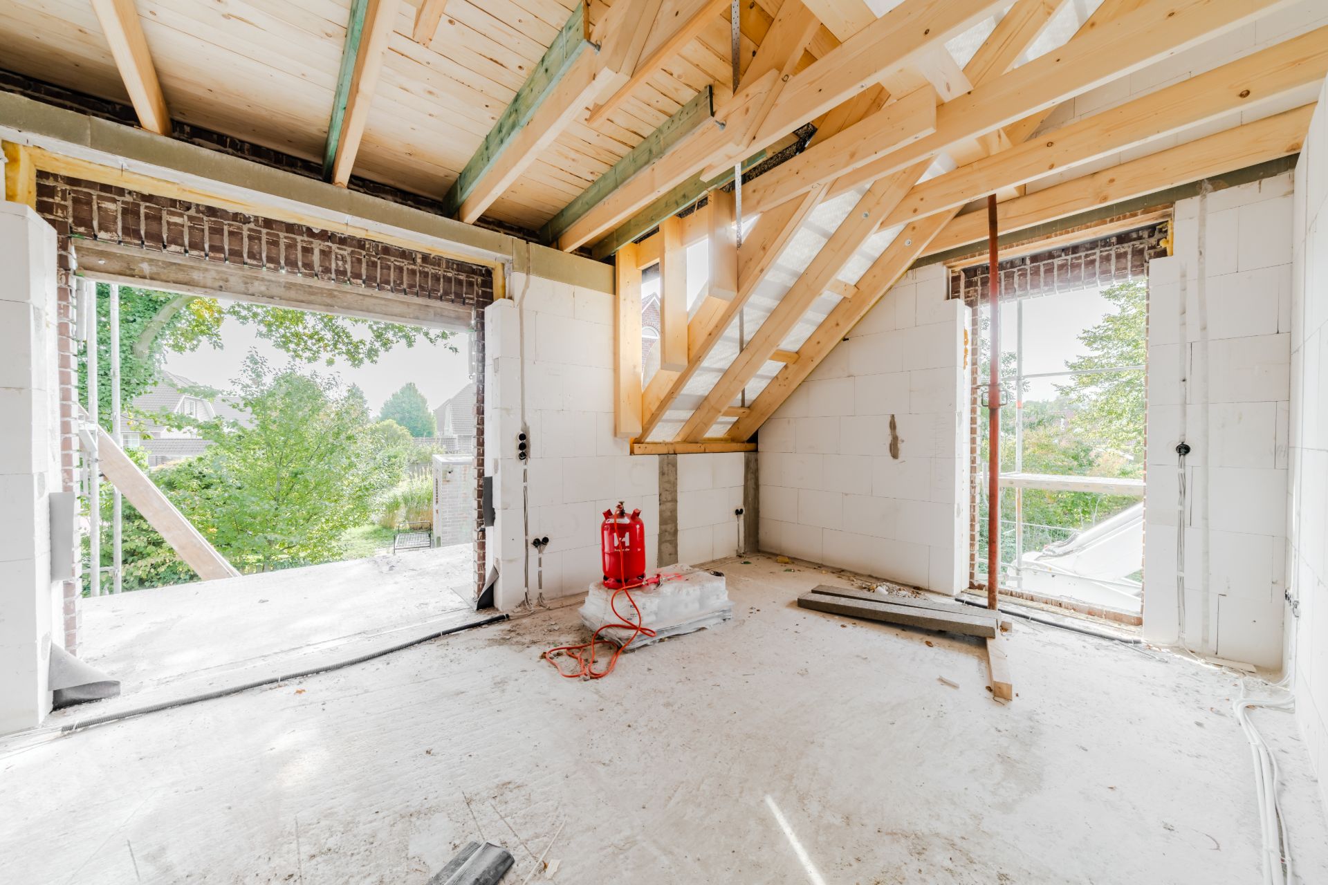 Heller Raum in einem Haus im Rohbau mit offenem Dachstuhl und großen Fensteröffnungen.