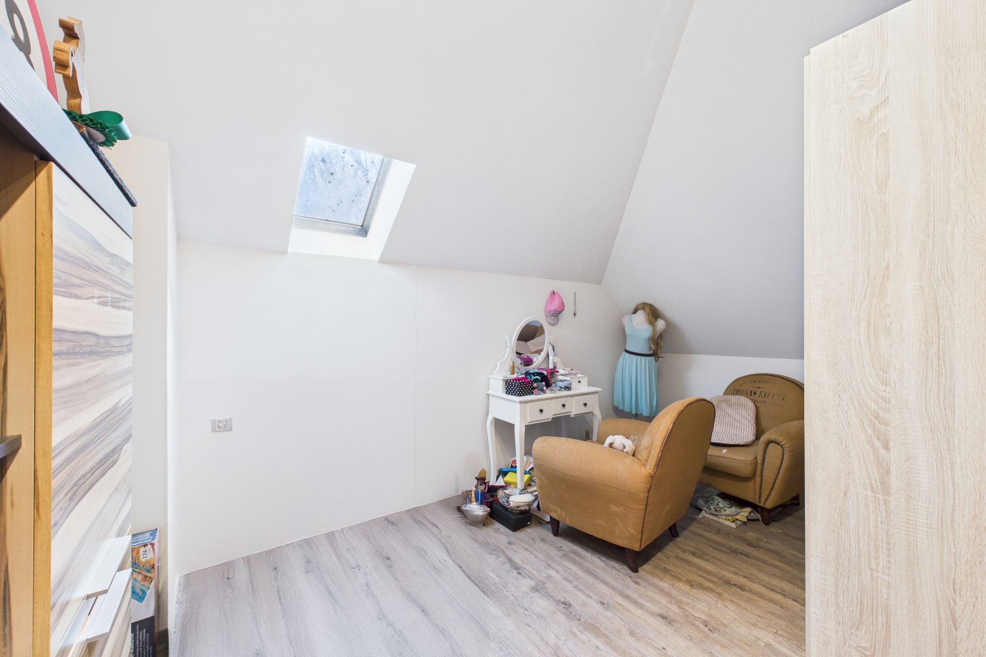 Kleines Zimmer mit Dachschräge, Sessel, Frisierkommode und Dachfenster.