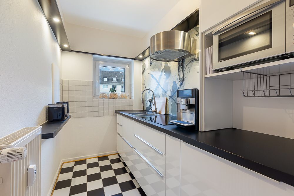 Moderne, schmale Küche mit kariertem Boden, weißen Schränken und Fenster am Ende.