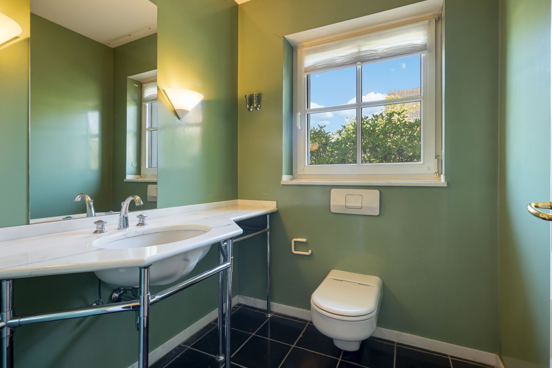 Modernes Badezimmer mit grün gestrichenen Wänden, Fenster, Waschbecken und wandhängender Toilette.