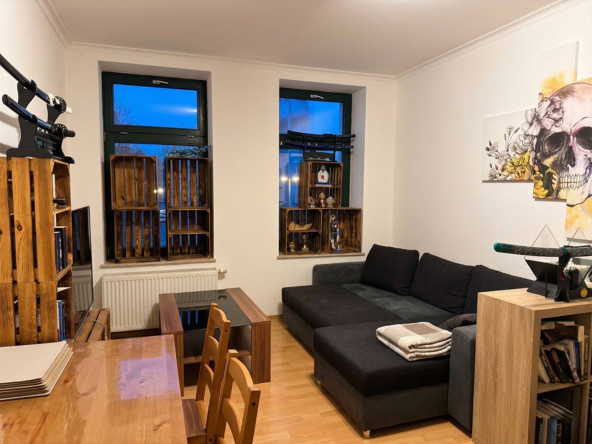 Wohnzimmer mit Ecksofa, Holztisch, Regalen aus Holzkisten und Wandbild mit Totenkopf.