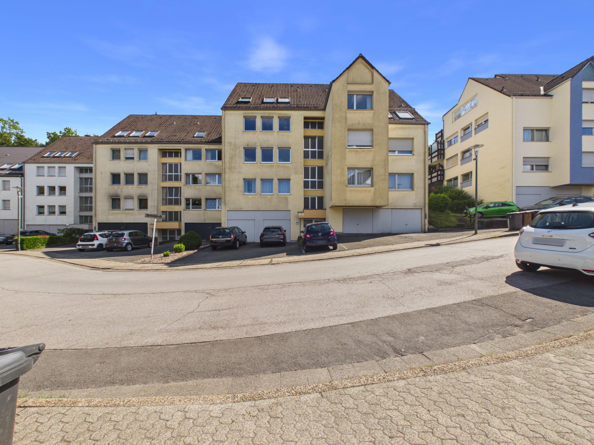 Mehrfamilienhaus mit mehreren Autos auf Parkplätzen vor dem Gebäude an einer ruhigen Straße.