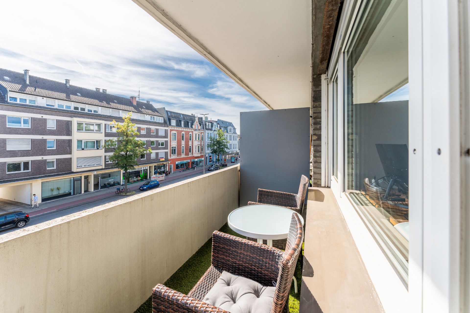 Balkon mit zwei Stühlen und rundem Tisch, Blick auf eine Straße mit Wohnhäusern.