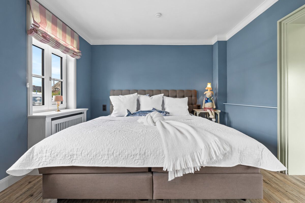 Schlafzimmer mit großem Bett, blauer Wand, Fenster und Nachttischlampe.