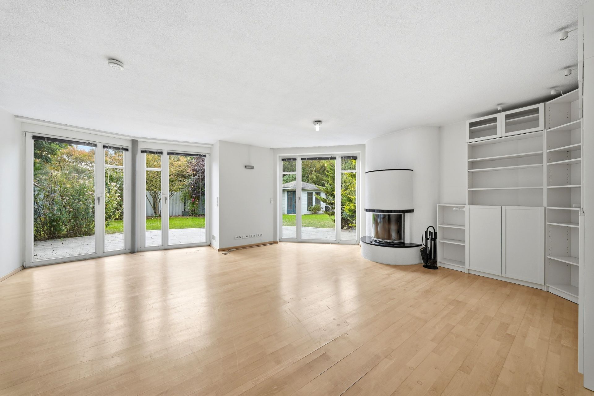 Helles Wohnzimmer mit Kamin, Einbauregalen, Parkettboden und bodentiefen Fenstern zum Garten.