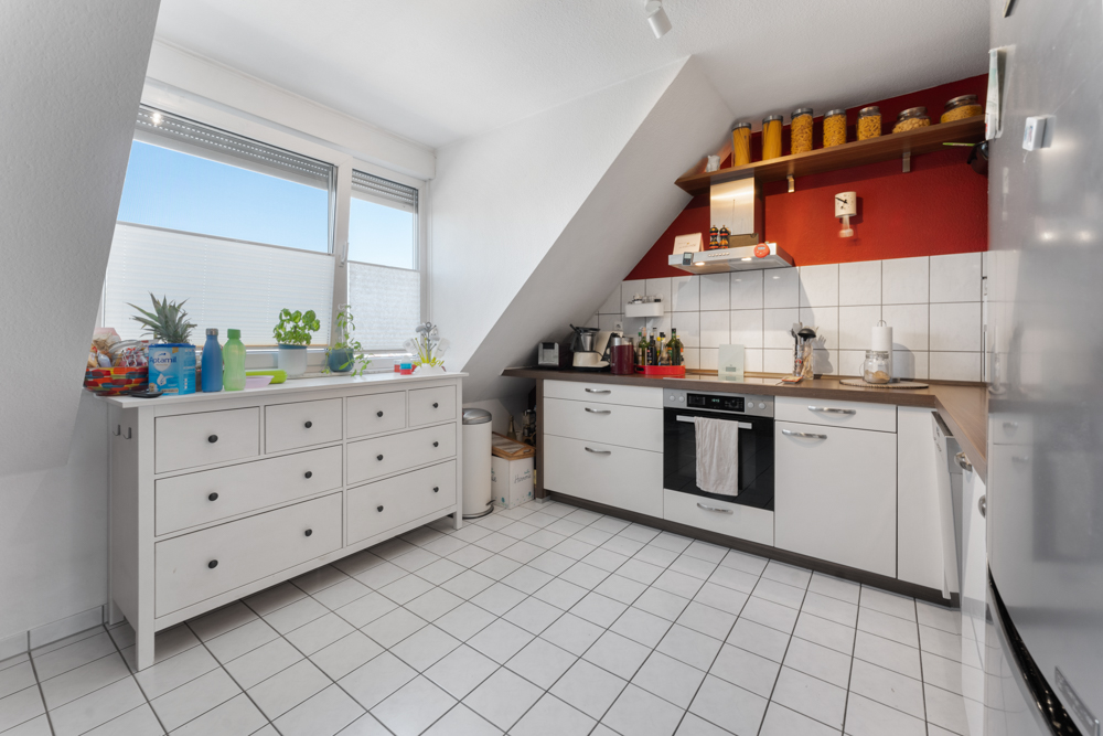 Helle Küche mit weißen Schränken, großem Fenster und roten Akzentwänden unter Dachschräge.