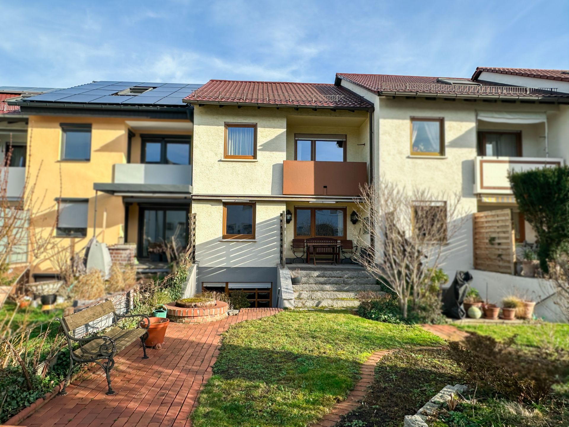 Reihenhaus mit Garten, Terrasse und Sitzbank, Weg aus roten Steinen führt zum Eingang.