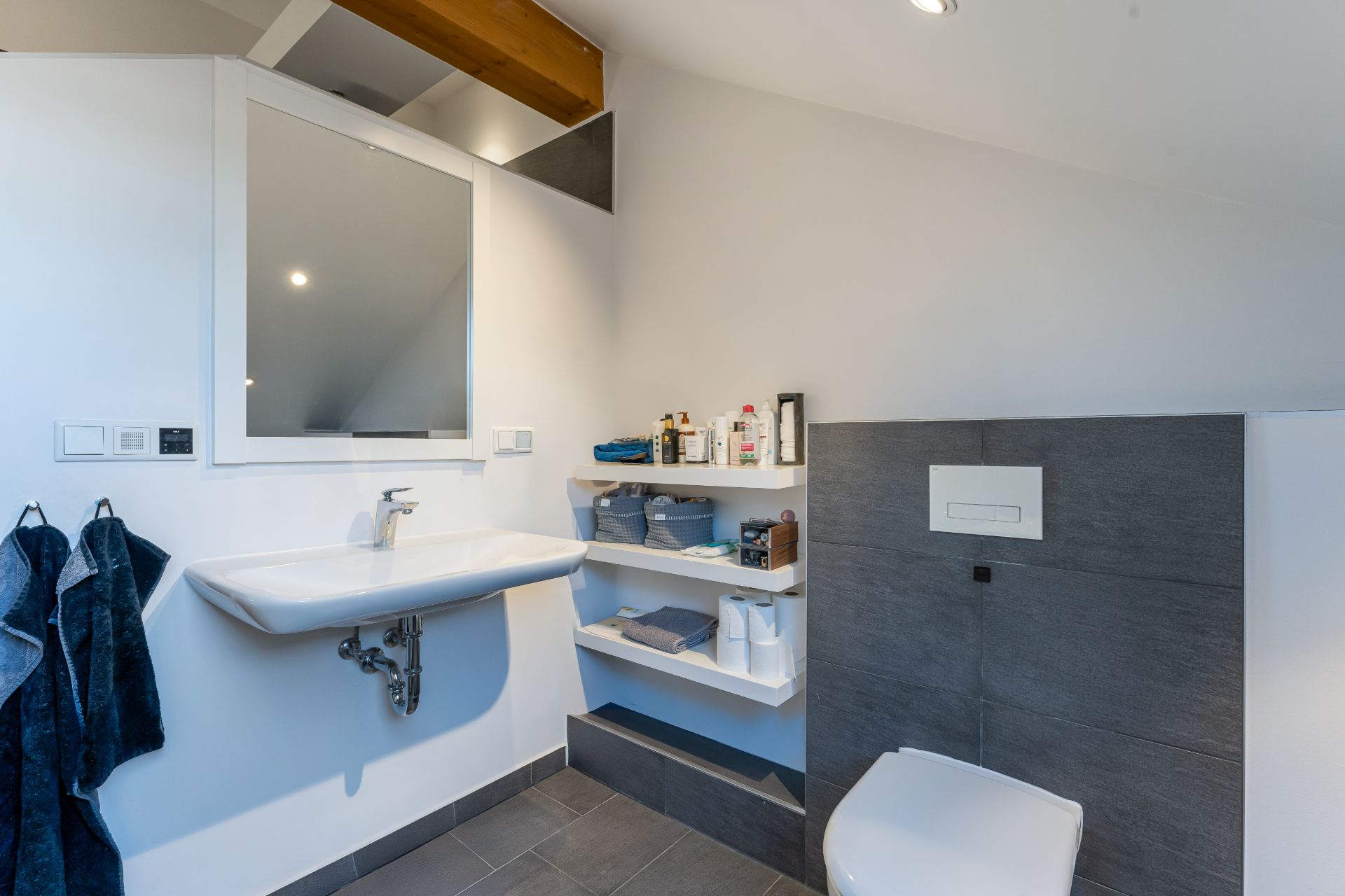 Modernes Badezimmer mit Wandwaschbecken, Spiegel, Regal und WC.