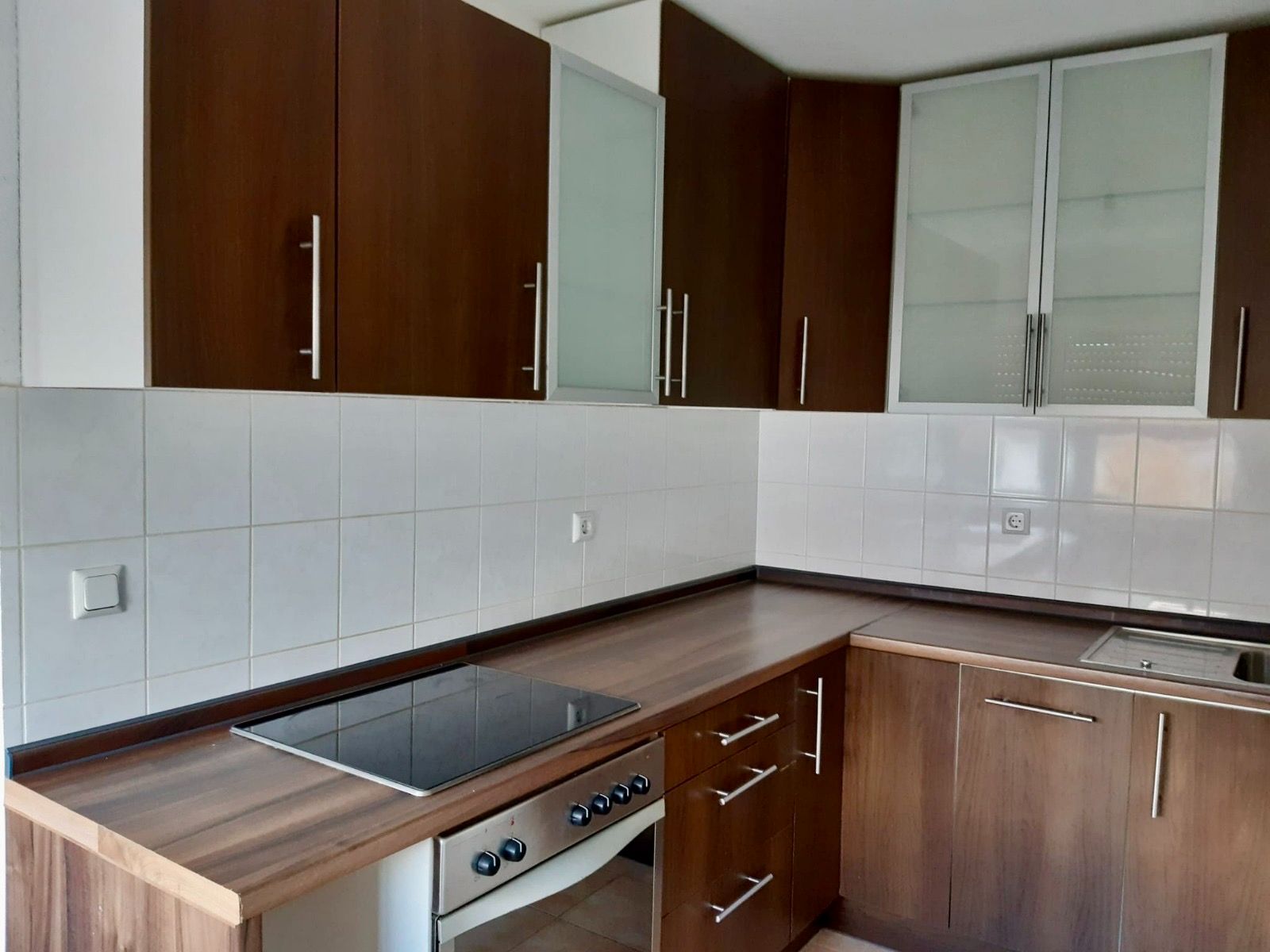 Moderne Küche mit dunklen Holzschränken, Elektroherd und Spüle.