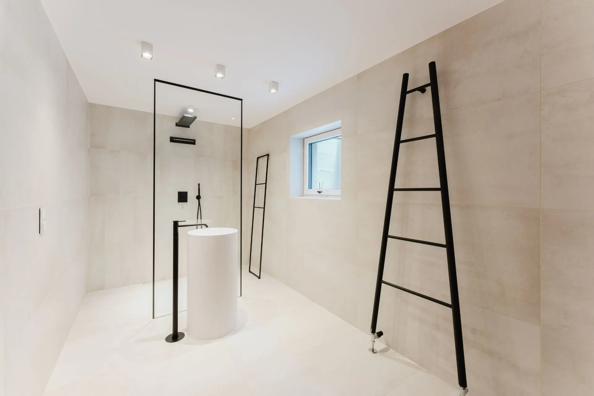 Modernes, helles Badezimmer mit Dusche, freistehendem Waschbecken und schwarzen Leiter-Handtuchhaltern.