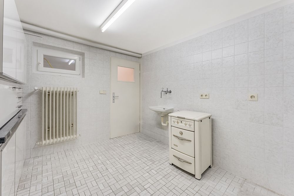 Heller Raum mit Fliesenboden, kleinem Waschbecken, Heizkörper und weißem Herd.