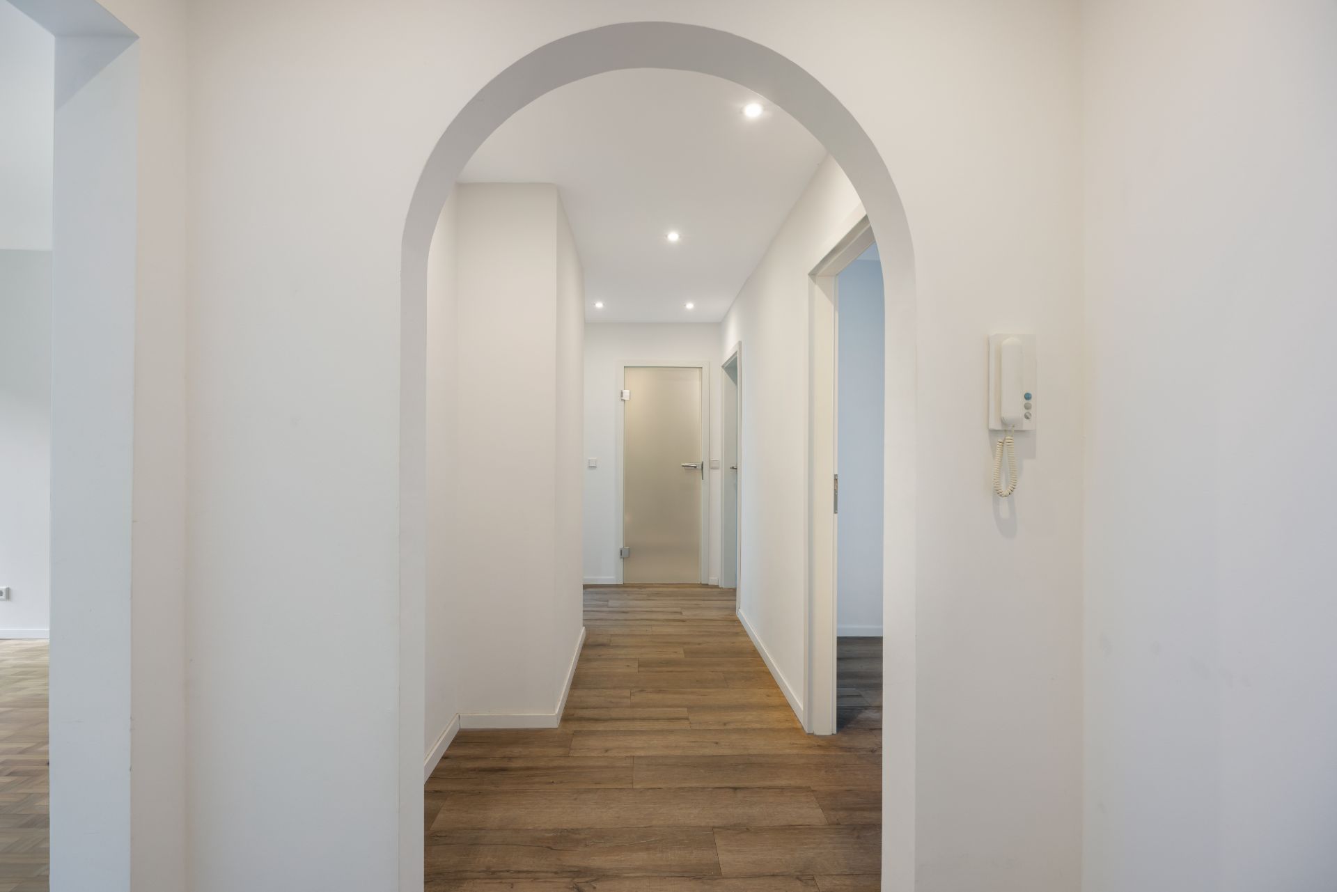 Heller Flur mit Rundbogen, Holzboden und mehreren Türen, Wände weiß gestrichen.