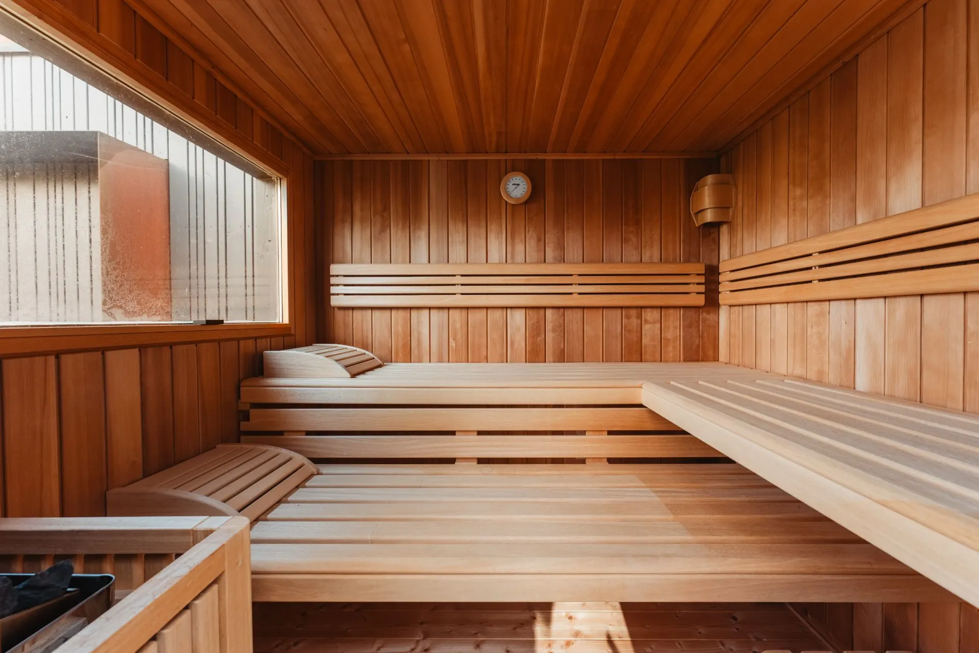 Innenansicht einer Holzsauna mit Bänken, Fenster und Wanduhr.