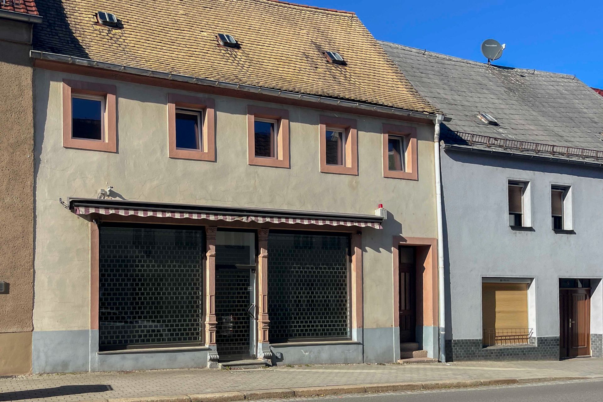 Zweistöckiges Wohnhaus mit vier Fenstern oben, großen Schaufenstern und Eingangstür unten.