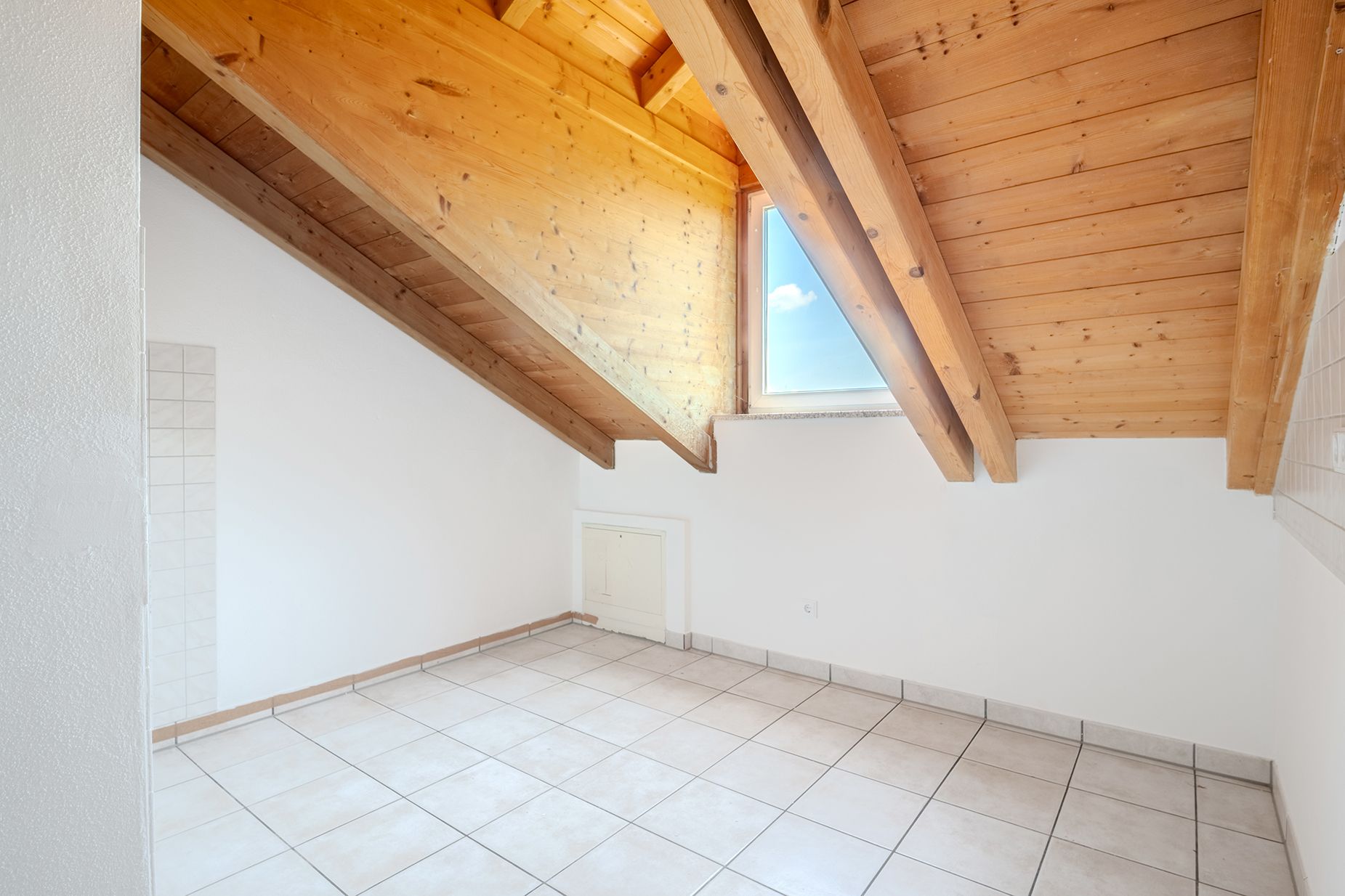 Heller Raum mit schräger Holzdecke, Fliesenboden und Dachfenster.