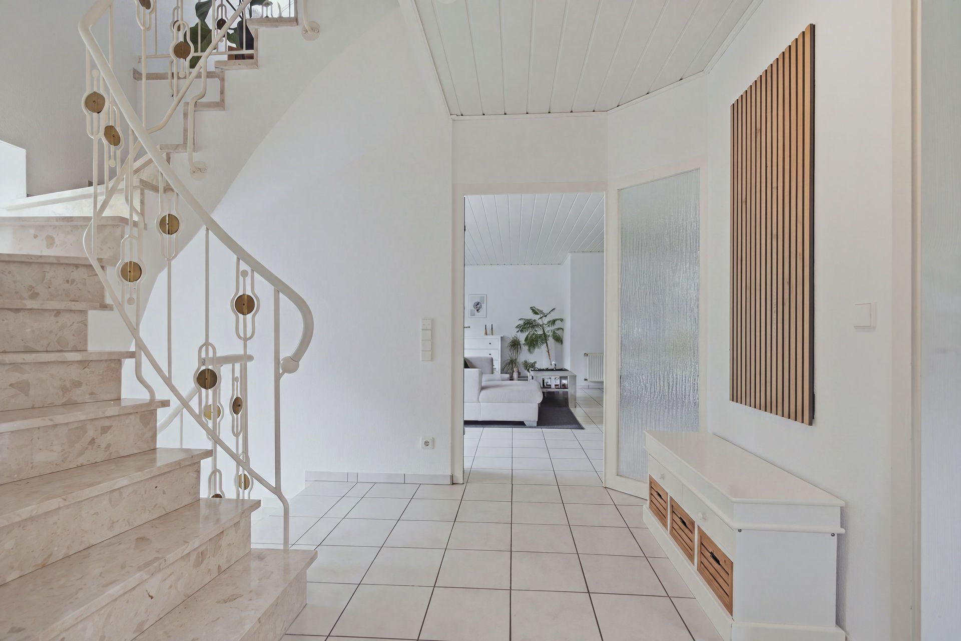Heller Flur mit Marmortreppe, Fliesenboden und Blick ins Wohnzimmer.