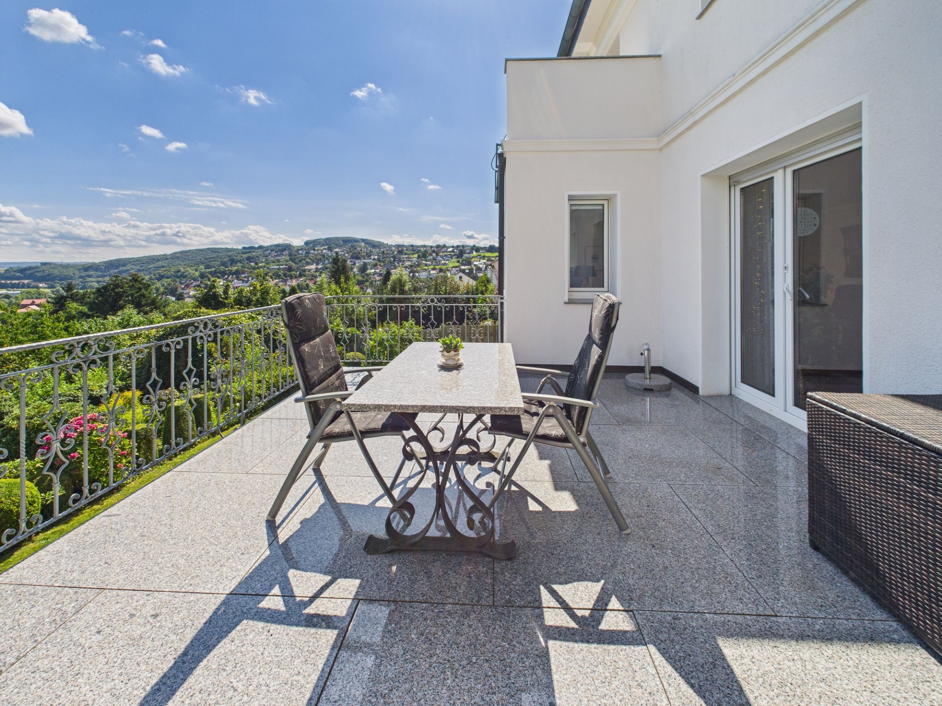 Große Terrasse mit Tisch, Stühlen und Ausblick auf grüne Hügel und Gärten.