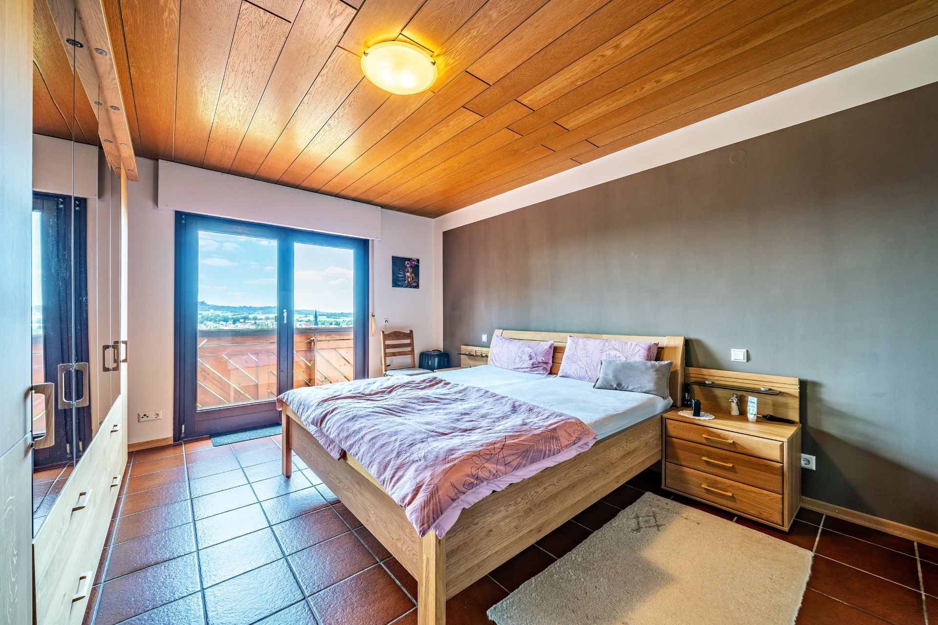 Schlafzimmer mit Doppelbett, Kleiderschrank, Nachttisch und großem Fenster mit Blick nach draußen.