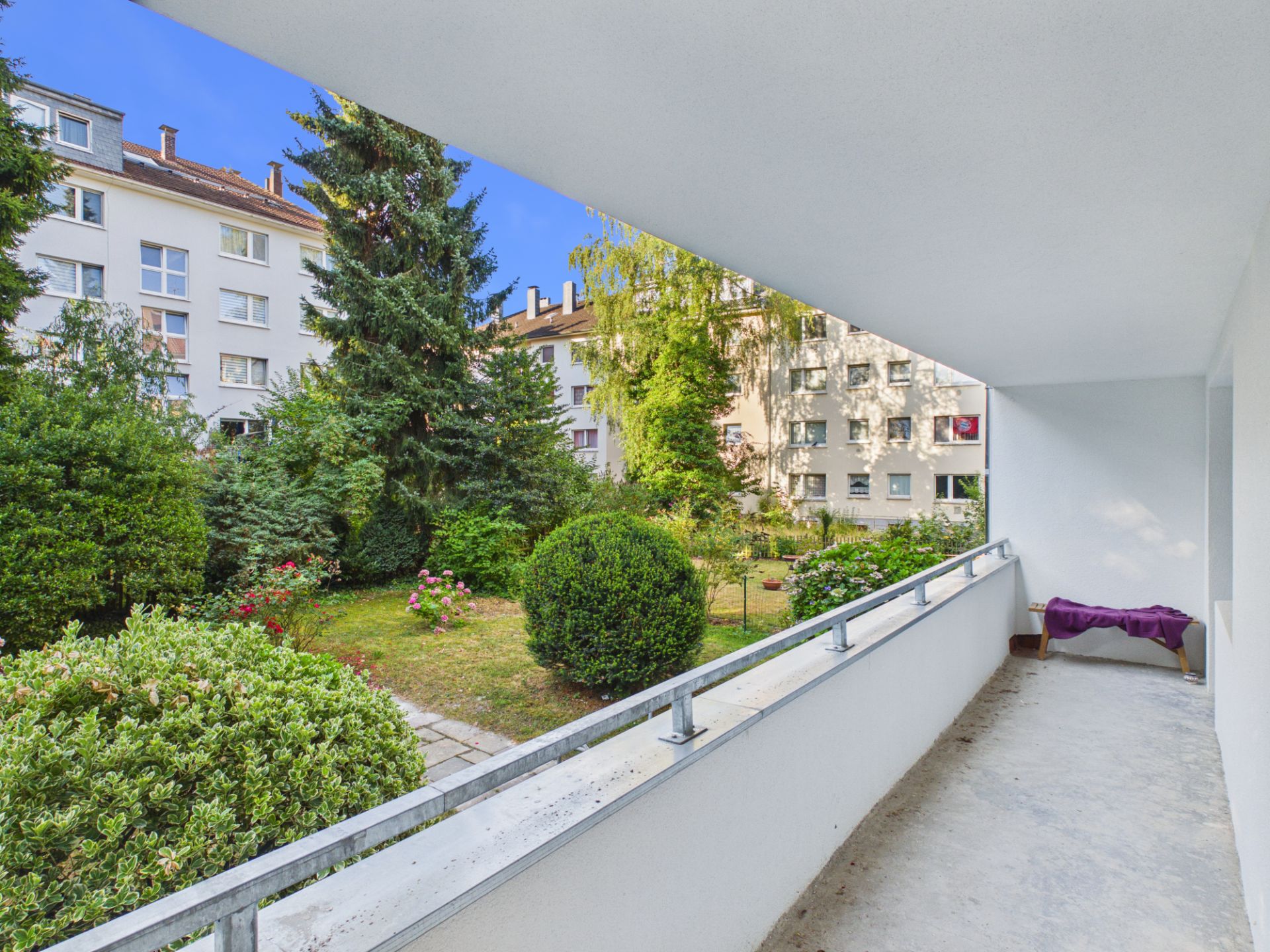 Balkon mit Blick auf einen grünen Garten und umliegende Wohngebäude.