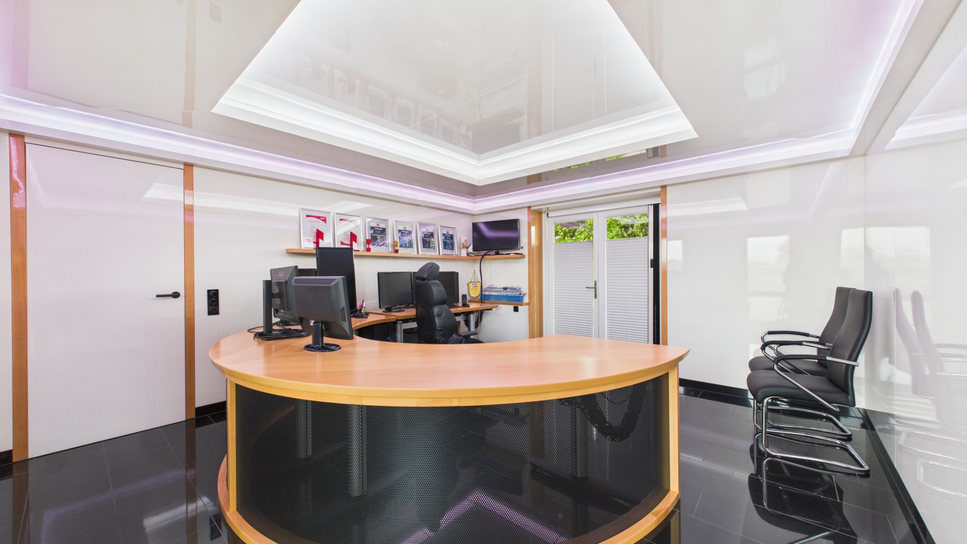 Modernes Büro mit rundem Schreibtisch, Computern, Stühlen und Wandbeleuchtung.