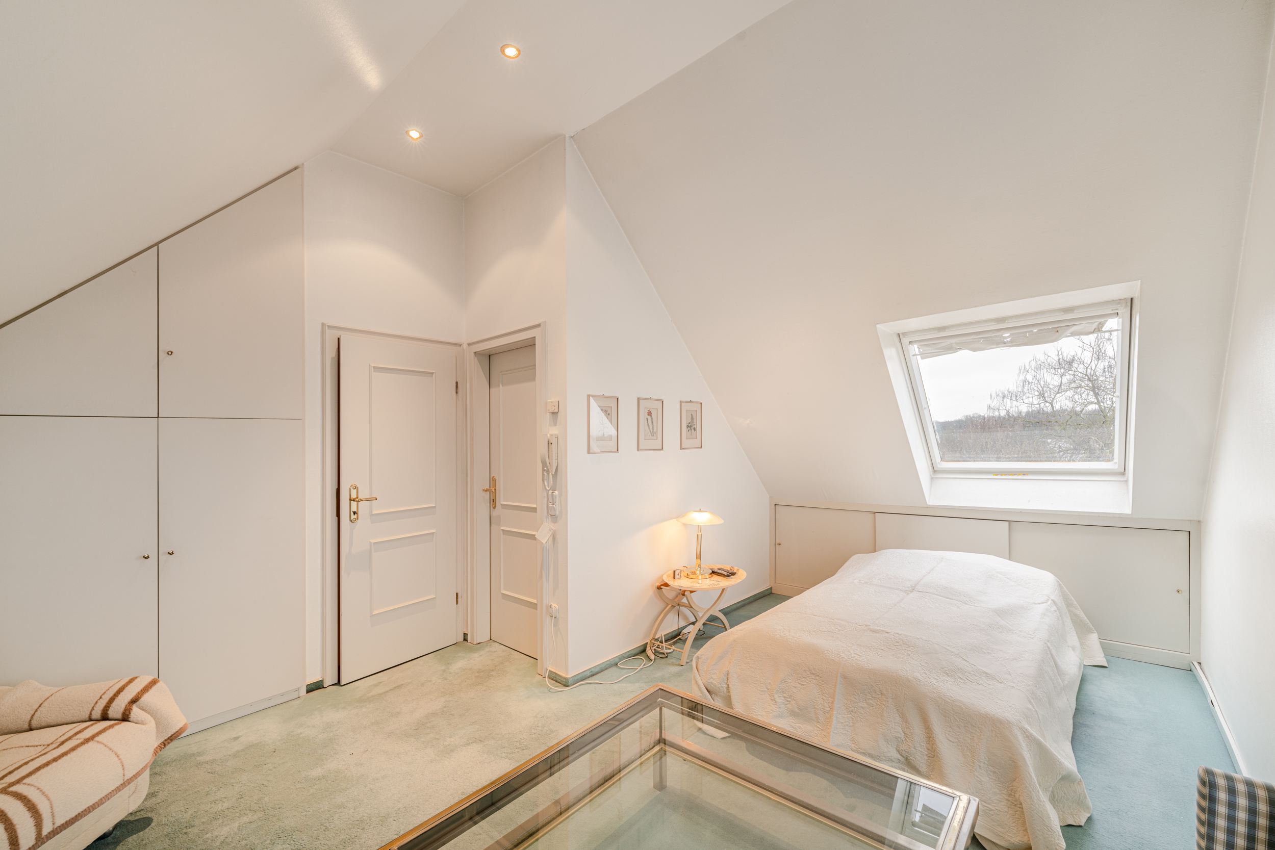 Helles Schlafzimmer mit Doppelbett, Dachfenster, Einbauschränken und Nachttischlampe.