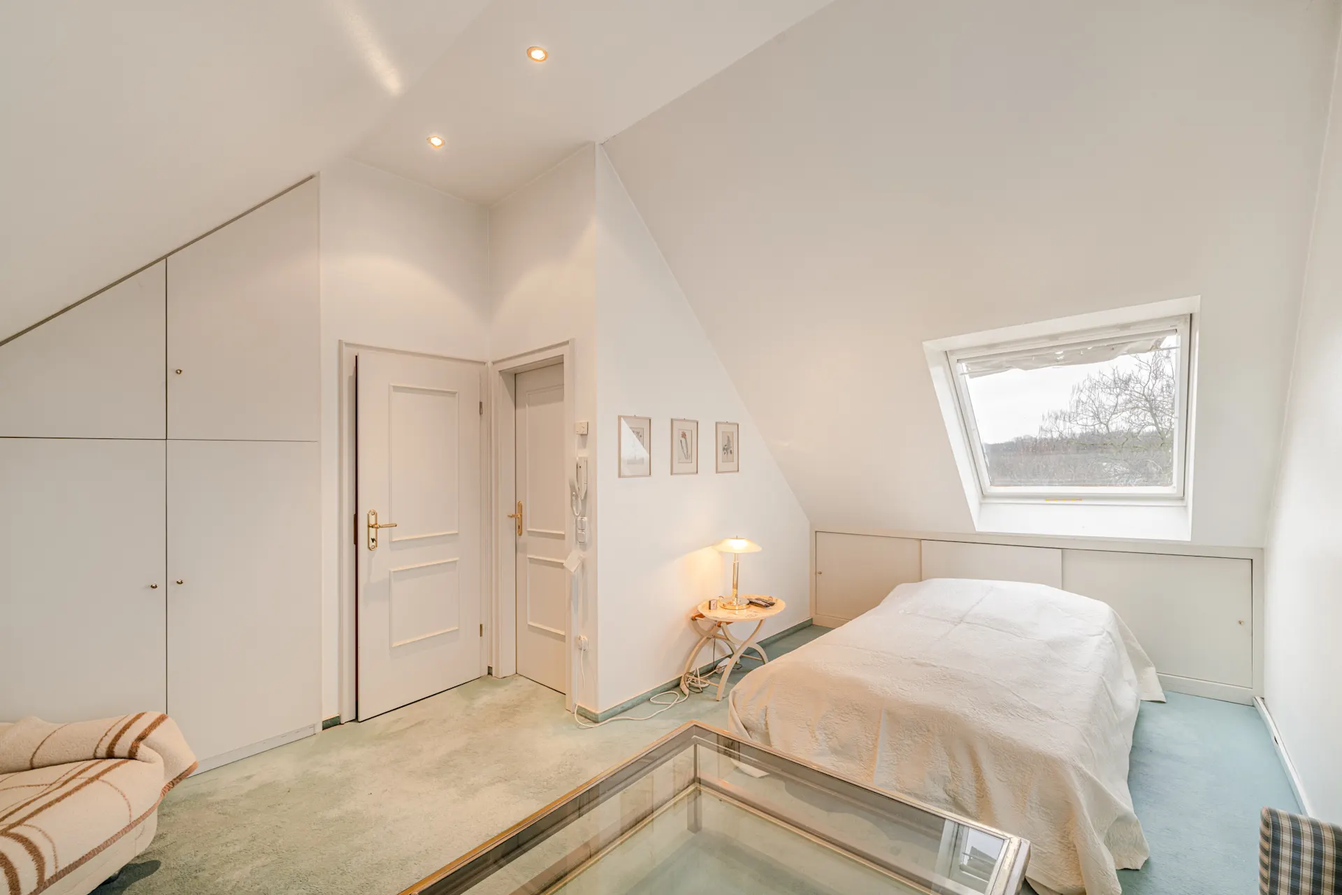 Helles Schlafzimmer mit Doppelbett, Dachfenster, Einbauschränken und Nachttischlampe.