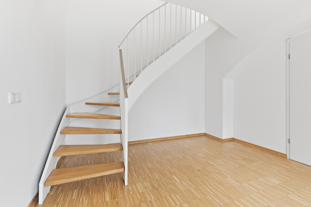 Moderne Holztreppe mit weißem Geländer in einem hellen Raum mit Parkettboden.