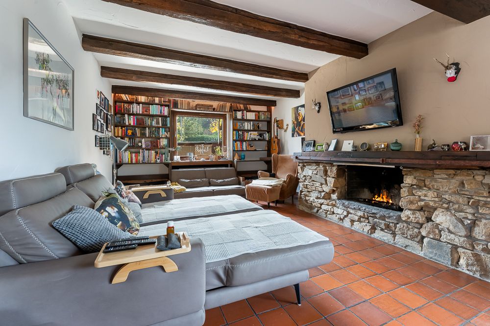 Gemütliches Wohnzimmer mit Kamin, Fernseher, Bücherregalen und Sofas vor einem Fenster.