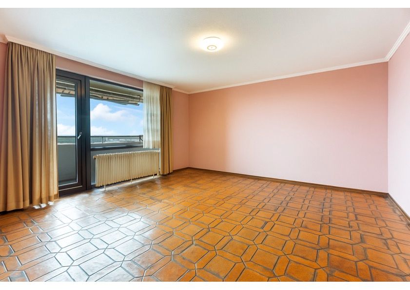 Leeres Zimmer mit rosa Wänden, braunen Fliesen und Zugang zu einem Balkon.