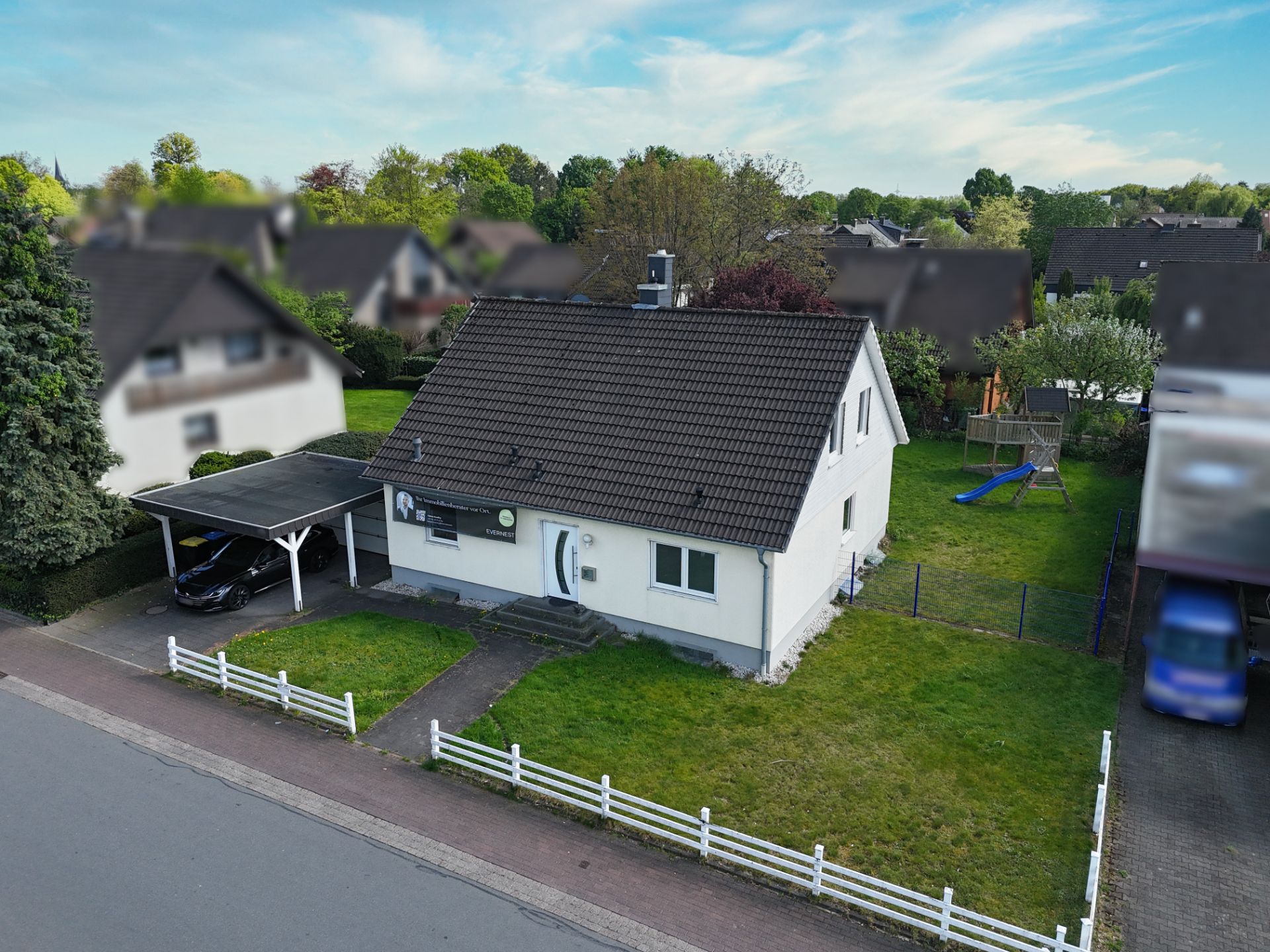 Einfamilienhaus mit Garten, Carport und Spielplatz im Vorgarten an einer ruhigen Straße.
