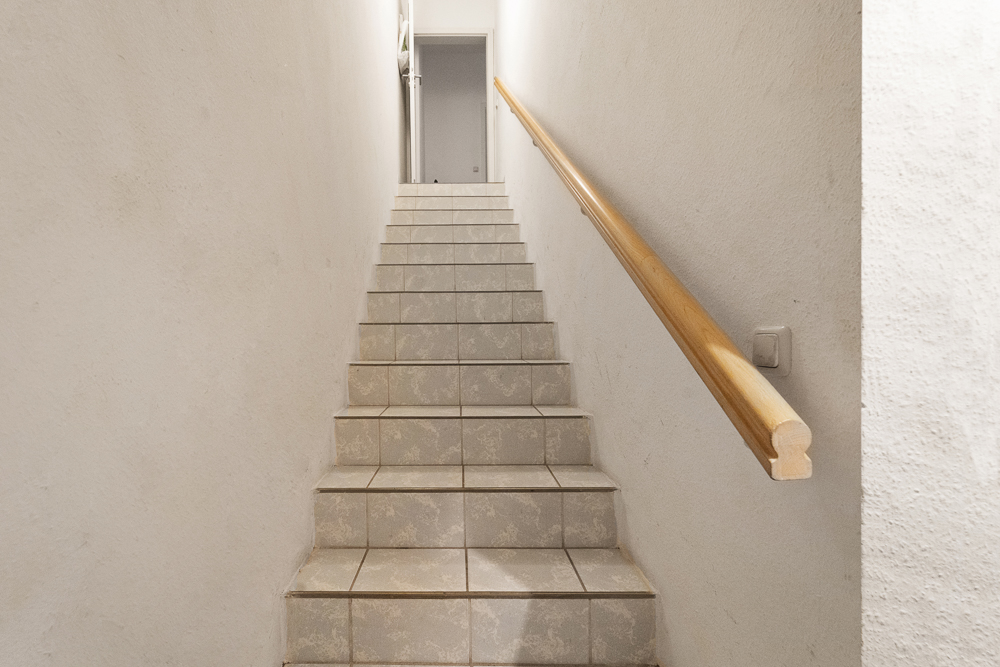 Geflieste Treppe mit Holzhandlauf und weißer Wand in einem Wohnhaus.