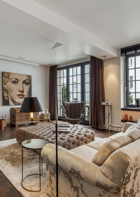 Modernes Wohnzimmer mit großem Fenster, Sofa, runder Ottomane und Gemälde an der Wand.