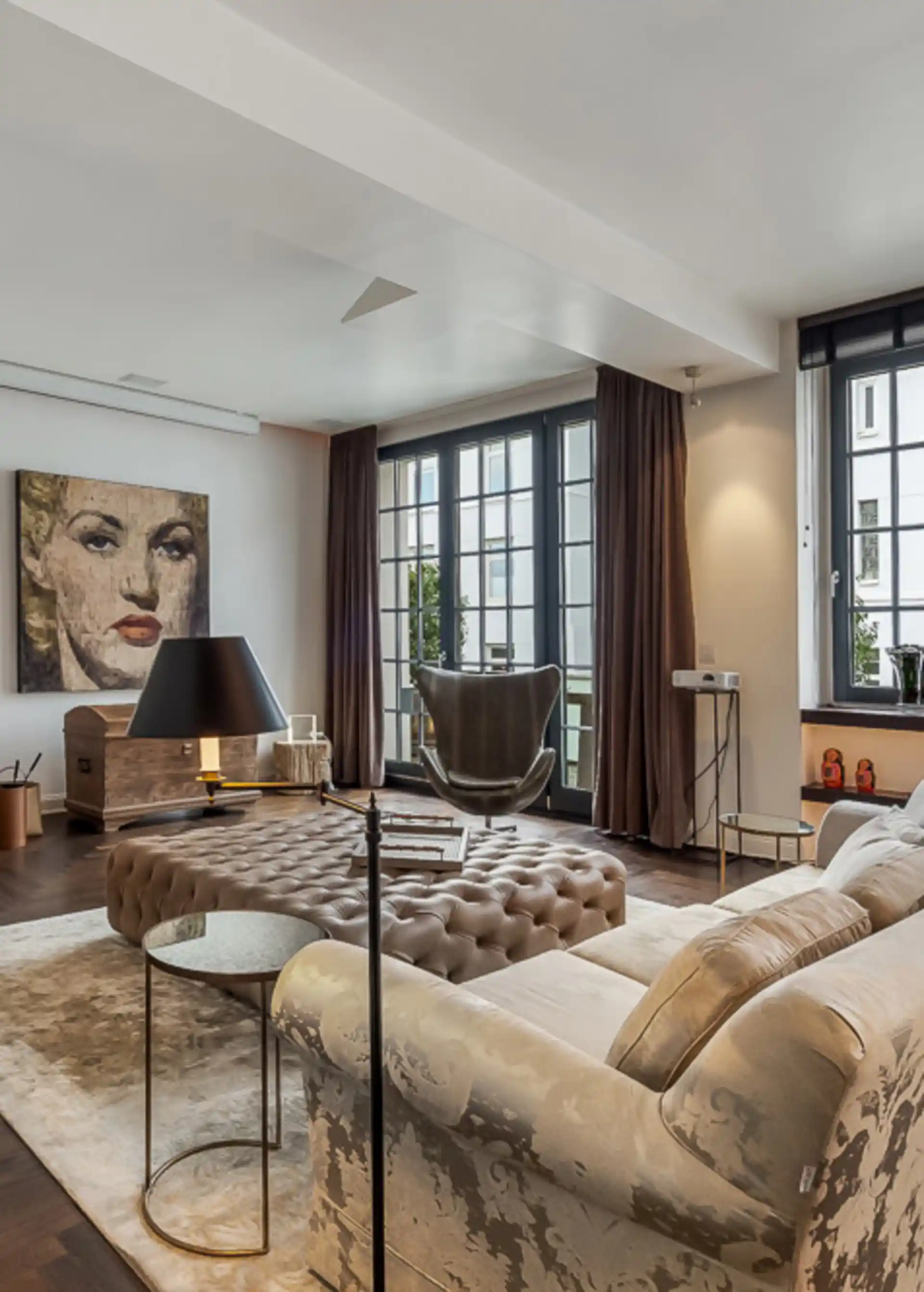 Modernes Wohnzimmer mit großem Fenster, Sofa, runder Ottomane und Gemälde an der Wand.