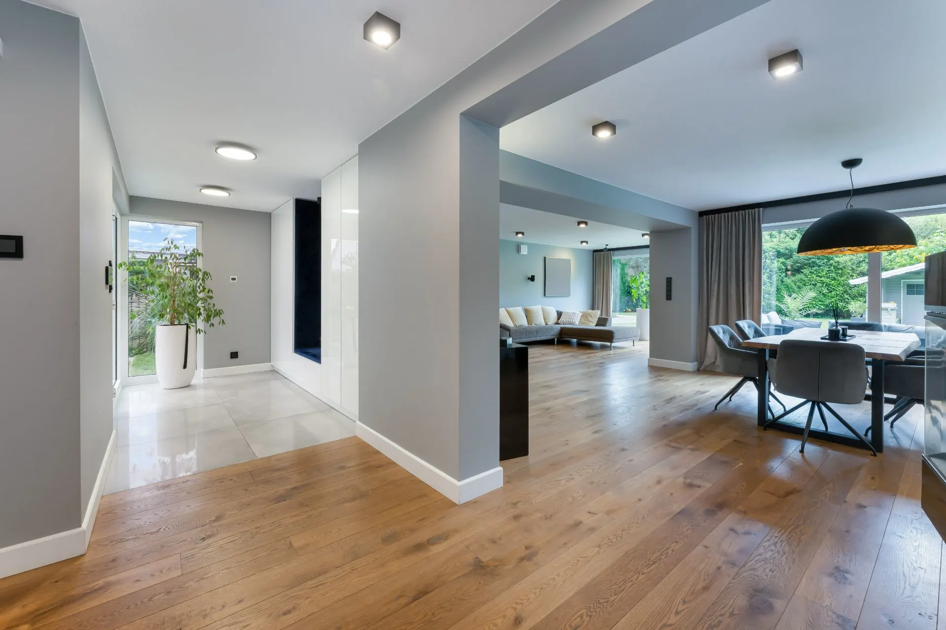 Modernes Wohnzimmer mit Holzboden, Essbereich, Sofa und großen Fenstern mit Blick ins Grüne.