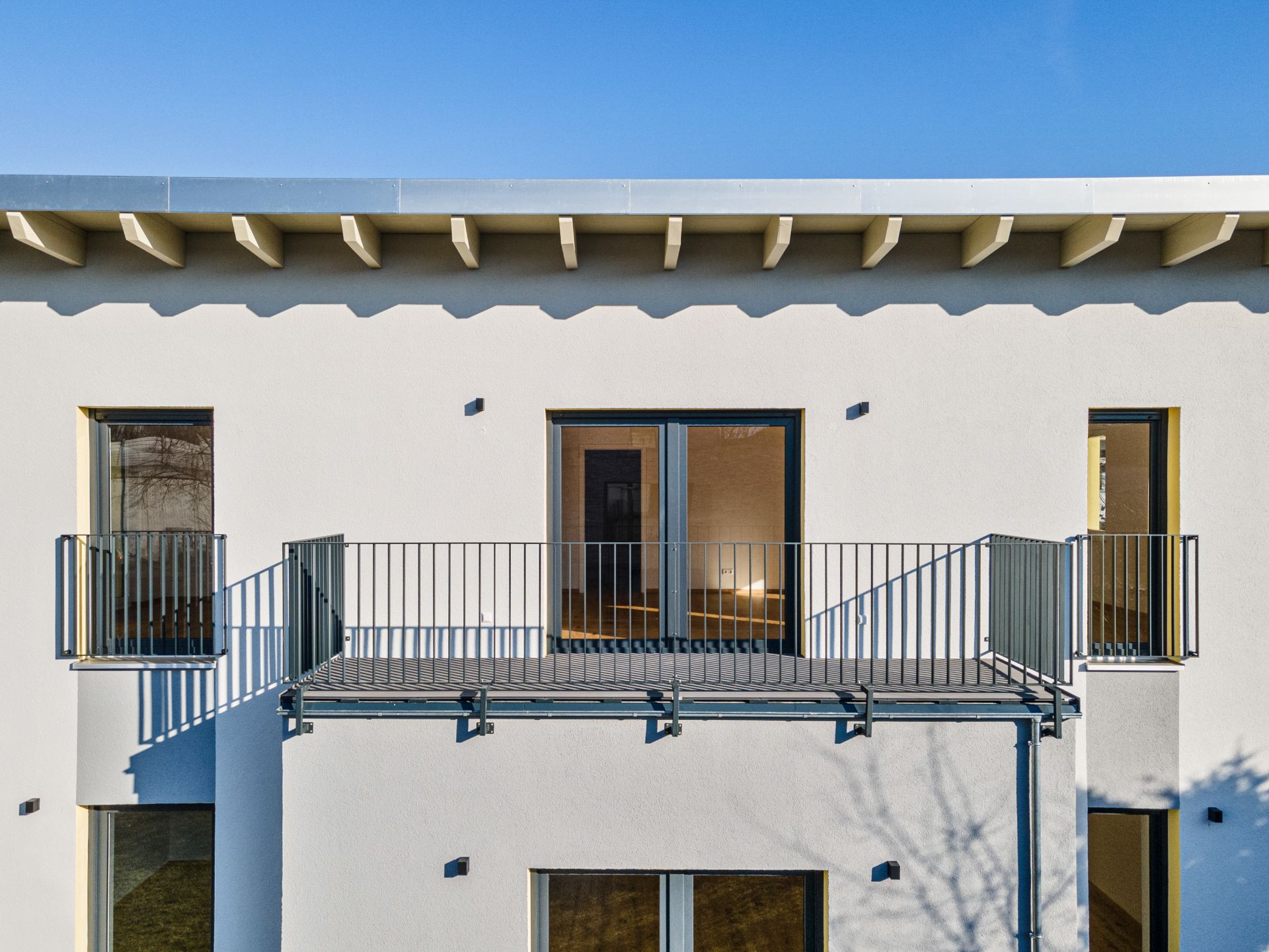 Fassade eines modernen Wohnhauses mit Balkon, großen Fenstern und blauem Himmel.