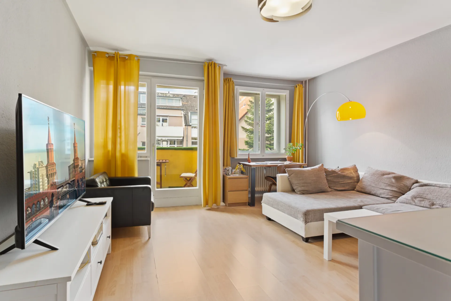 Modernes Wohnzimmer mit gelbem Vorhang, Sofa, Fernseher und Zugang zum Balkon.