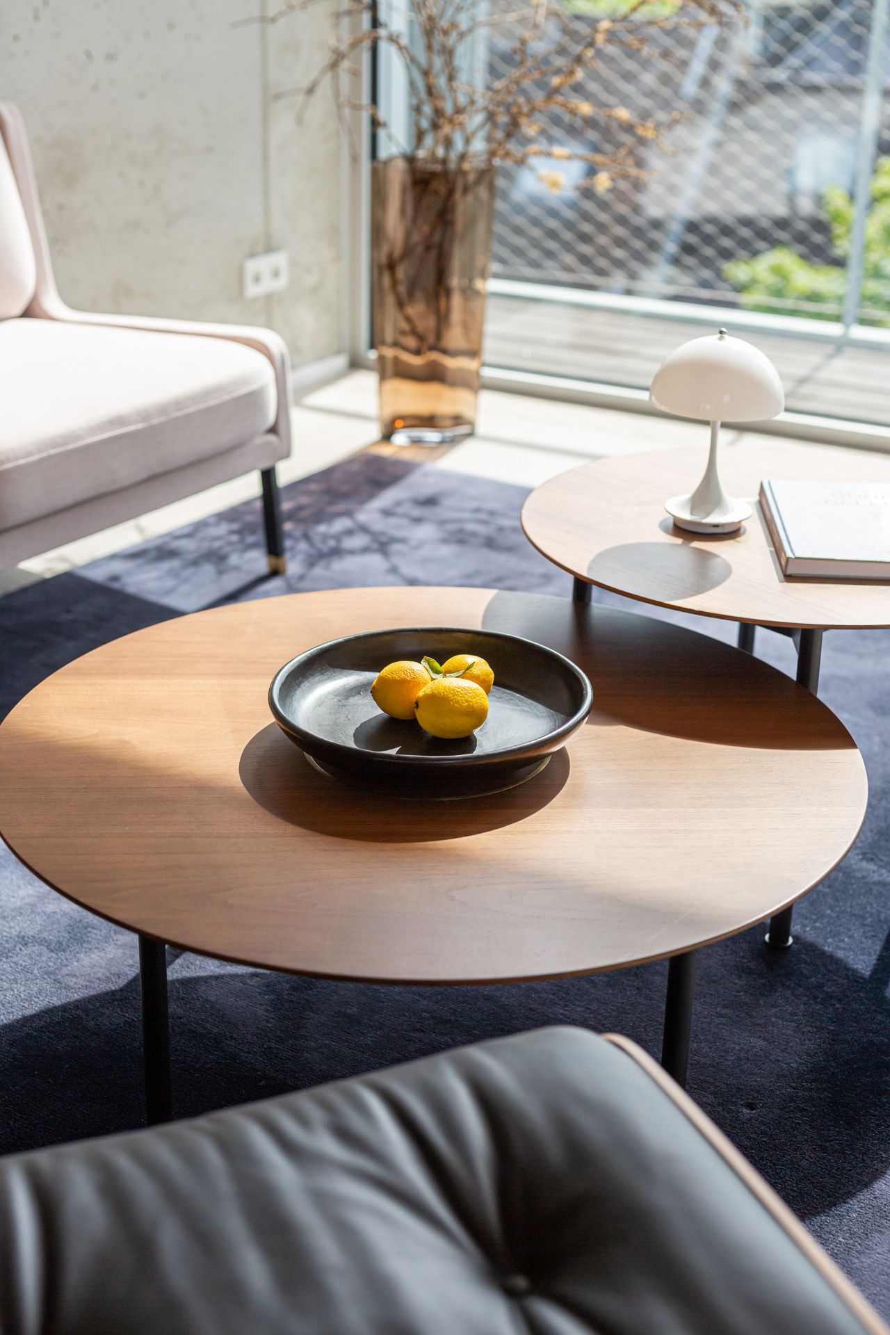 Wohnzimmer mit Holztisch, Schale mit Zitronen, Sessel und Fenster im Hintergrund.