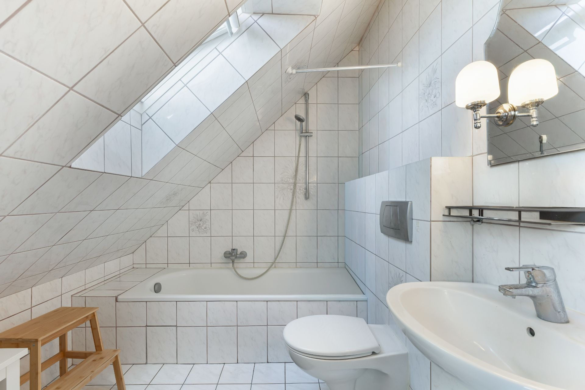 Helles Badezimmer mit Badewanne, Waschbecken, WC und Dachfenster in einem Raum mit Schräge.
