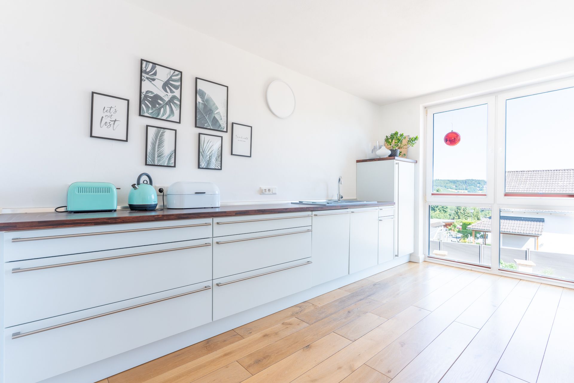 Helle moderne Küche mit weißen Schränken, Holzboden und großen Fenstern.
