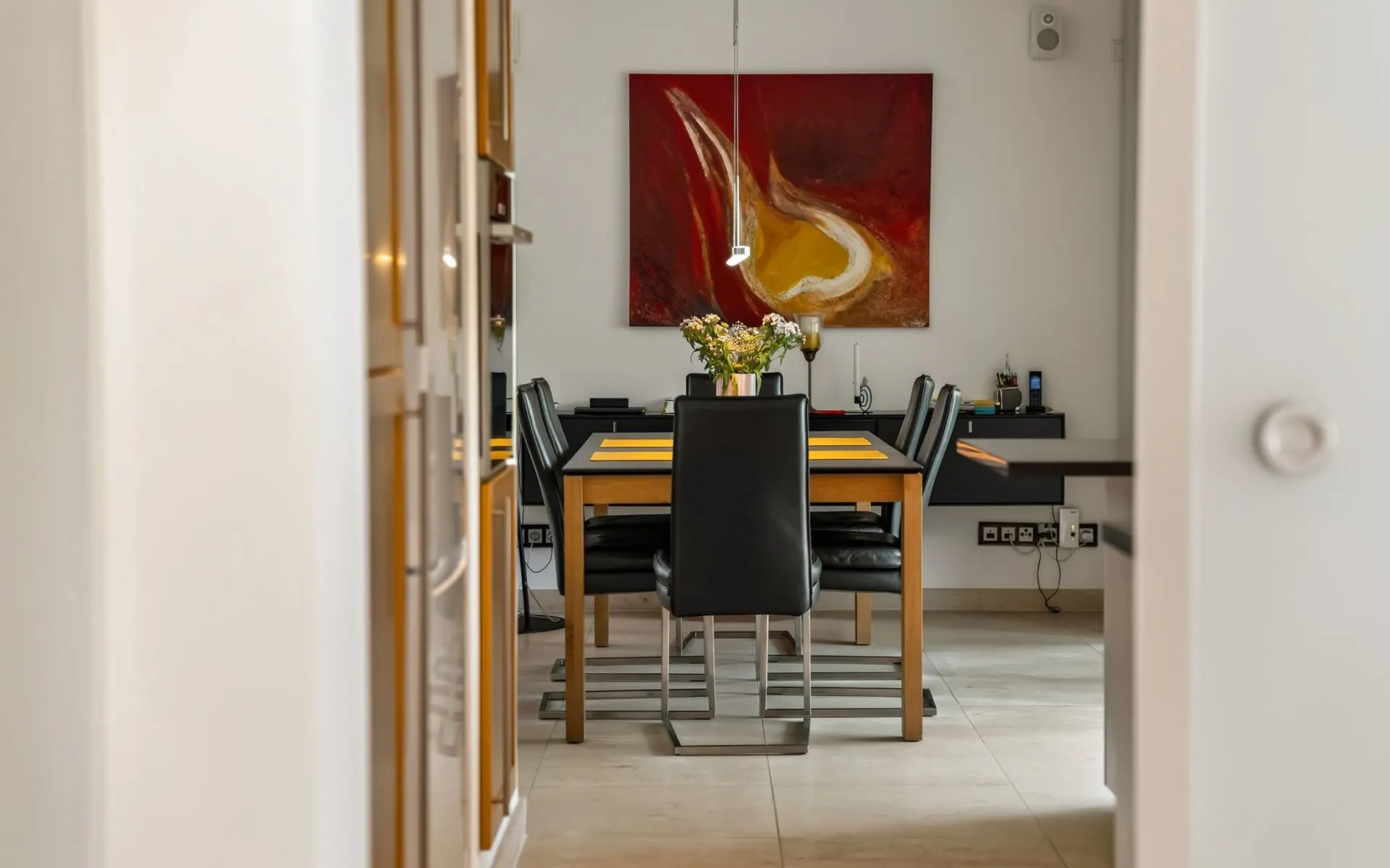Esszimmer mit Holztisch, schwarzen Stühlen und Blumen, abstraktes Gemälde an der Wand.