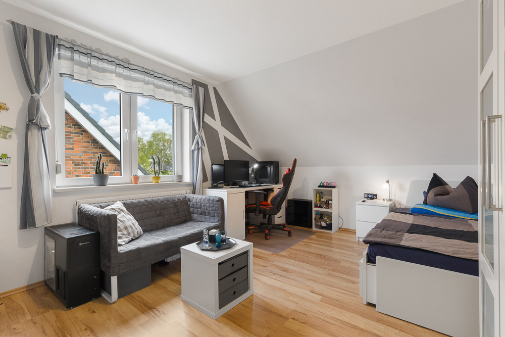 Helles Jugendzimmer mit Sofa, Schreibtisch, Bett und großem Fenster mit Vorhängen.