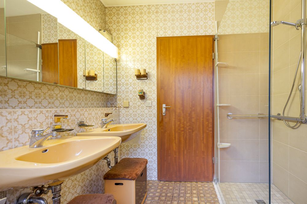 Badezimmer mit zwei Waschbecken, brauner Tür, Spiegeln und einer Dusche mit Haltegriff.