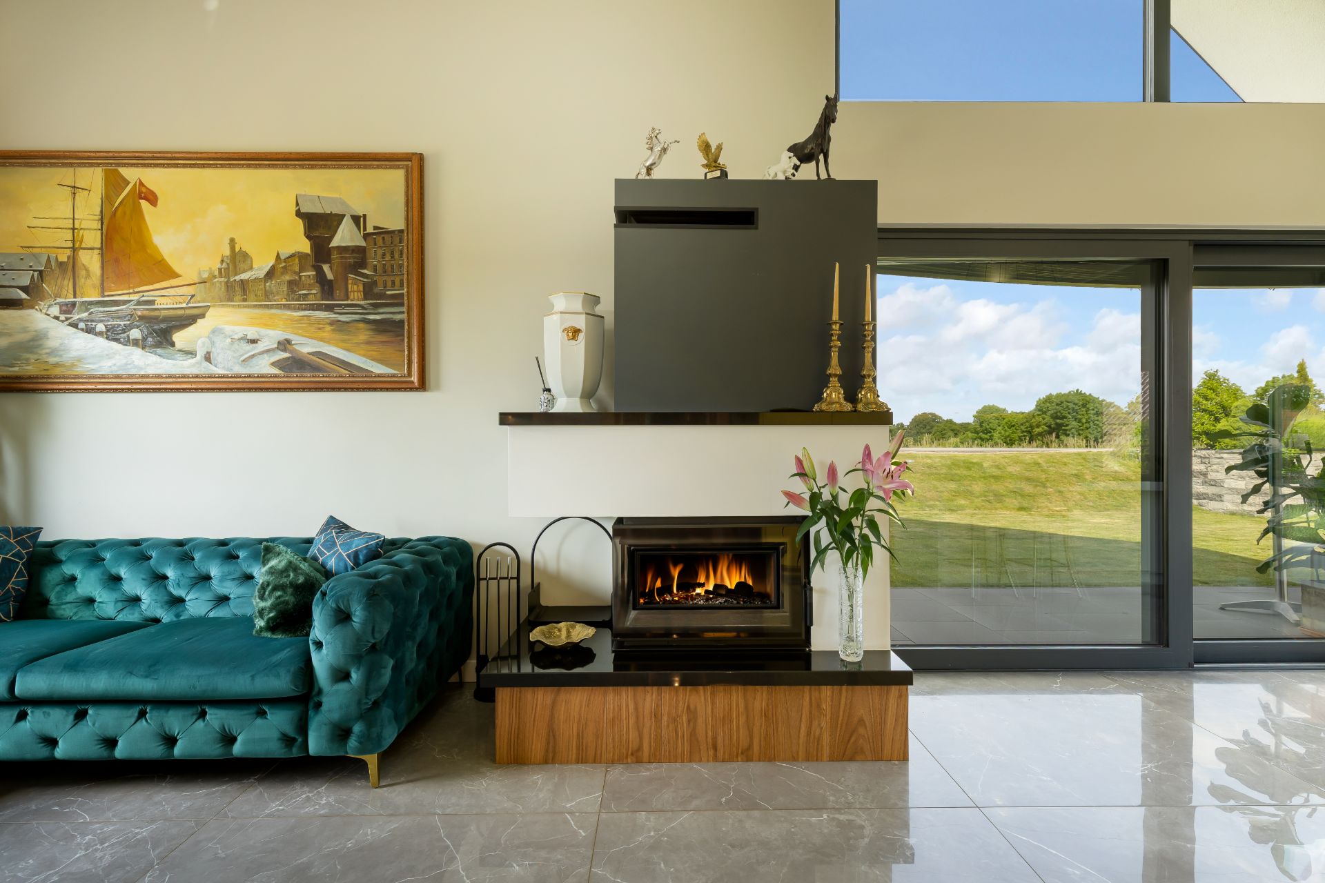 Wohnzimmer mit grünem Sofa, Kamin, Vase mit Blumen und großem Fenster zum Garten.