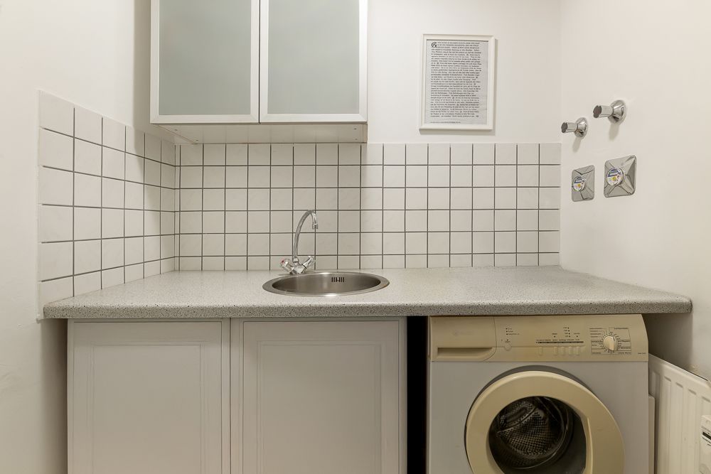 Hauswirtschaftsraum mit Waschmaschine, Spüle und weißen Fliesen an der Wand.