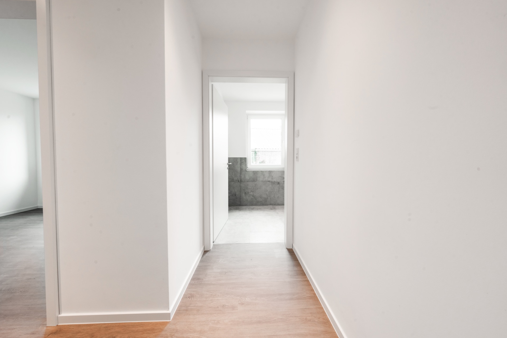Heller Flur mit Holzboden und Blick in ein Badezimmer mit Fenster.