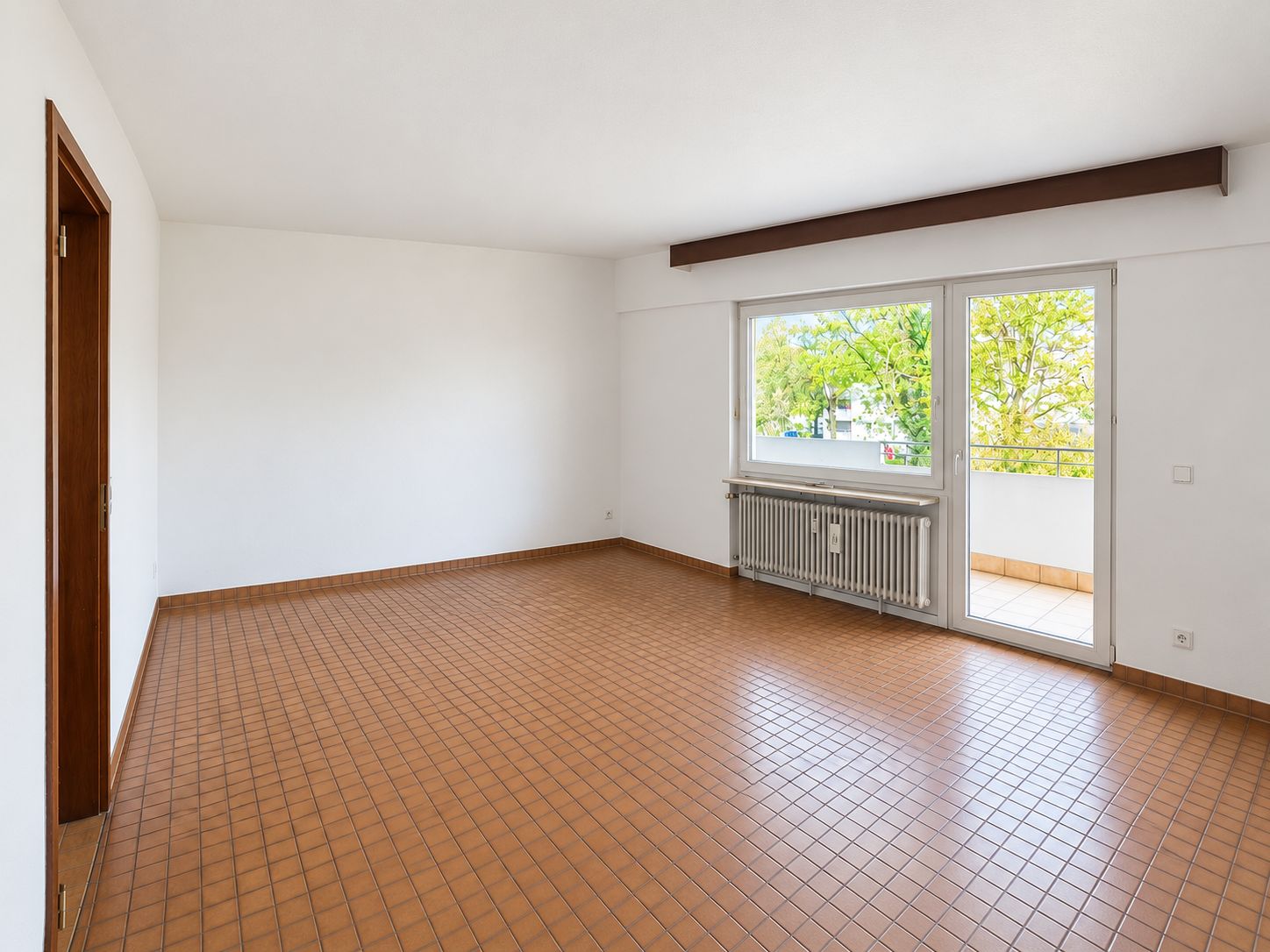 Leeres Zimmer mit braunen Fliesen, weißer Wand, Fenster und Tür zu einem Balkon.