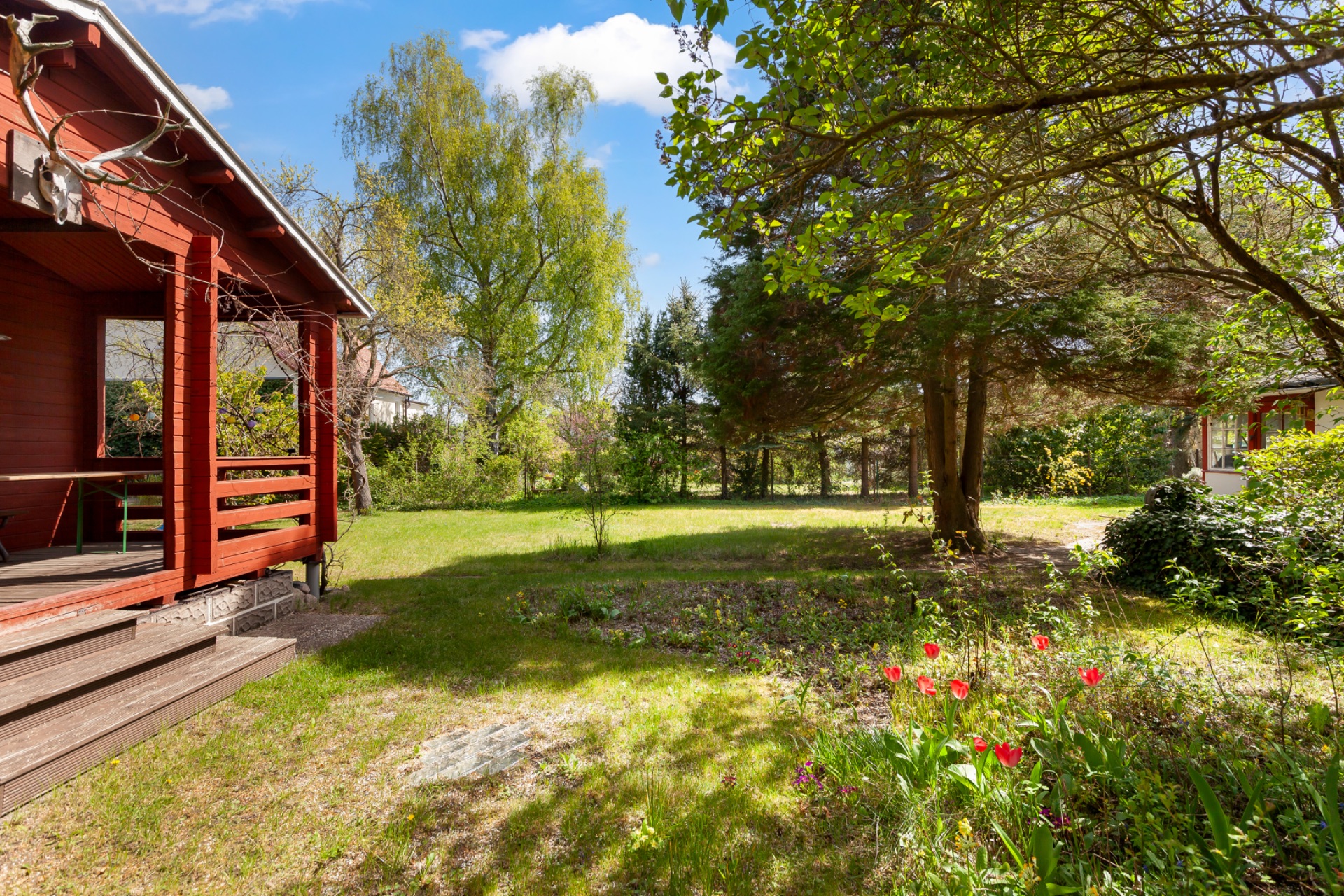 Garten mit Rasen, Bäumen, Blumenbeet und Holzveranda eines Hauses.