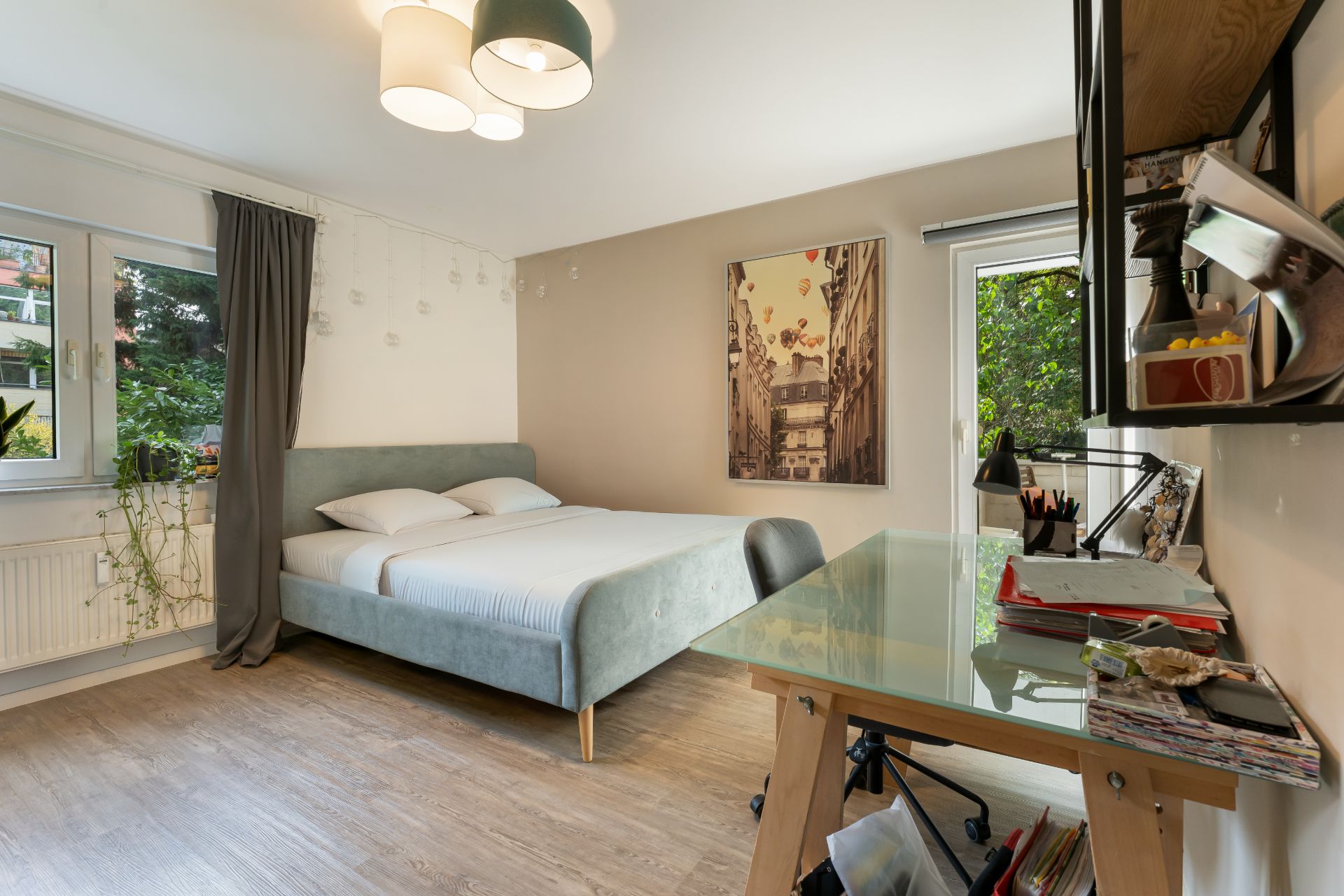 Modernes Schlafzimmer mit Doppelbett, Schreibtisch und großen Fenstern.